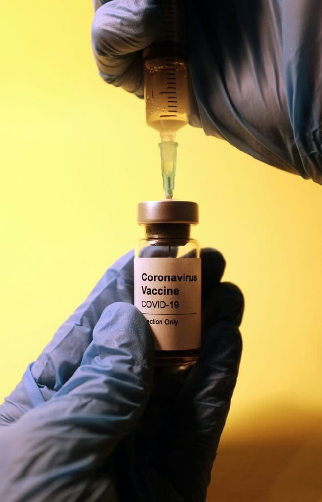 A vaccination needle being inserted into a vial, against a bright yellow background