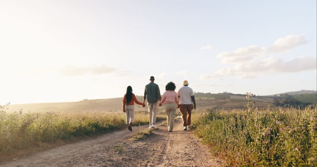 Four members of a family holding hands and walking down a dirt path in an open field.
