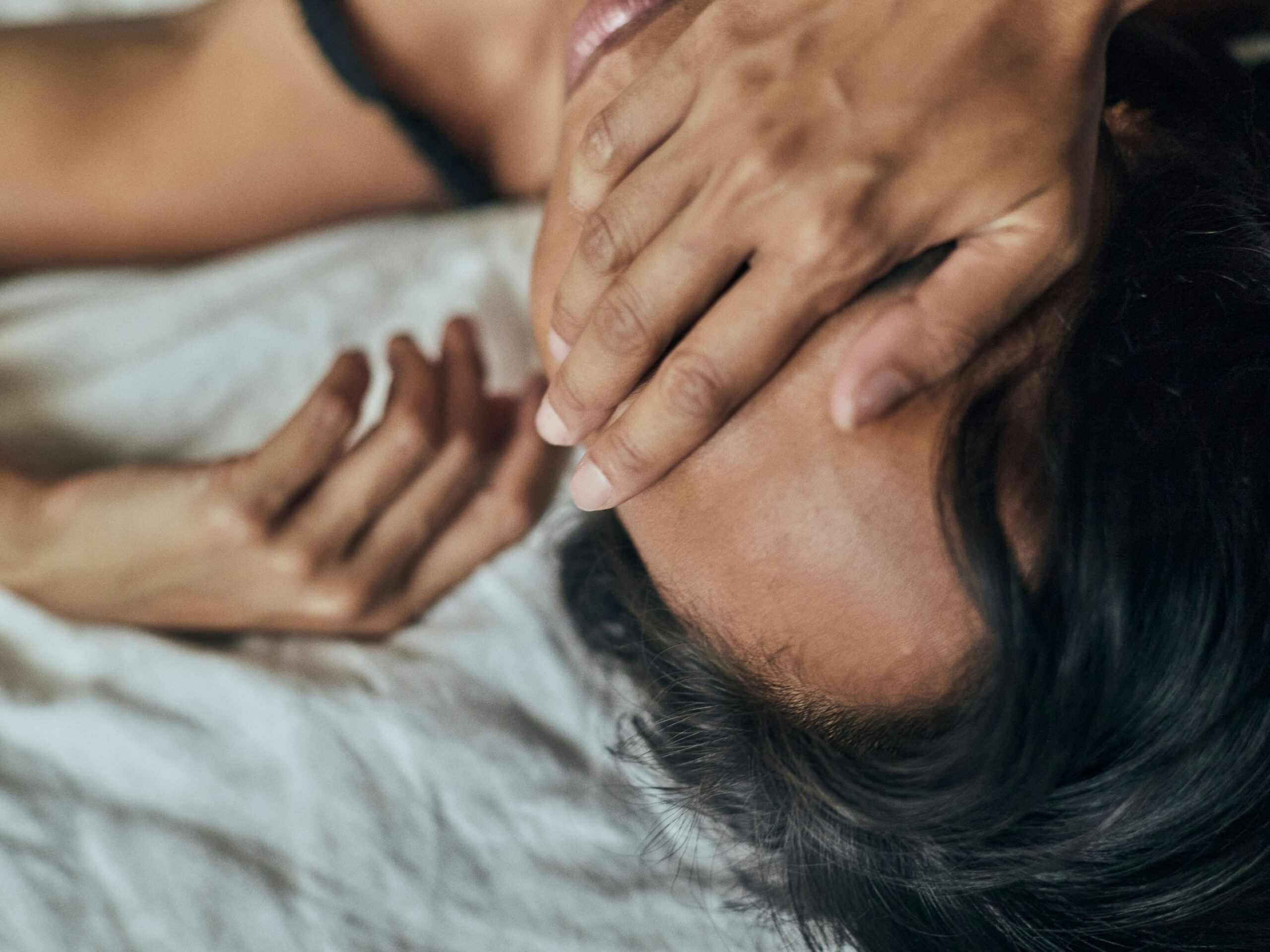 Woman lying on a bed with her hand covering her face.