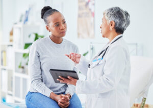 Middle-aged woman sitting on doctor's table while speaking with a woman physician.