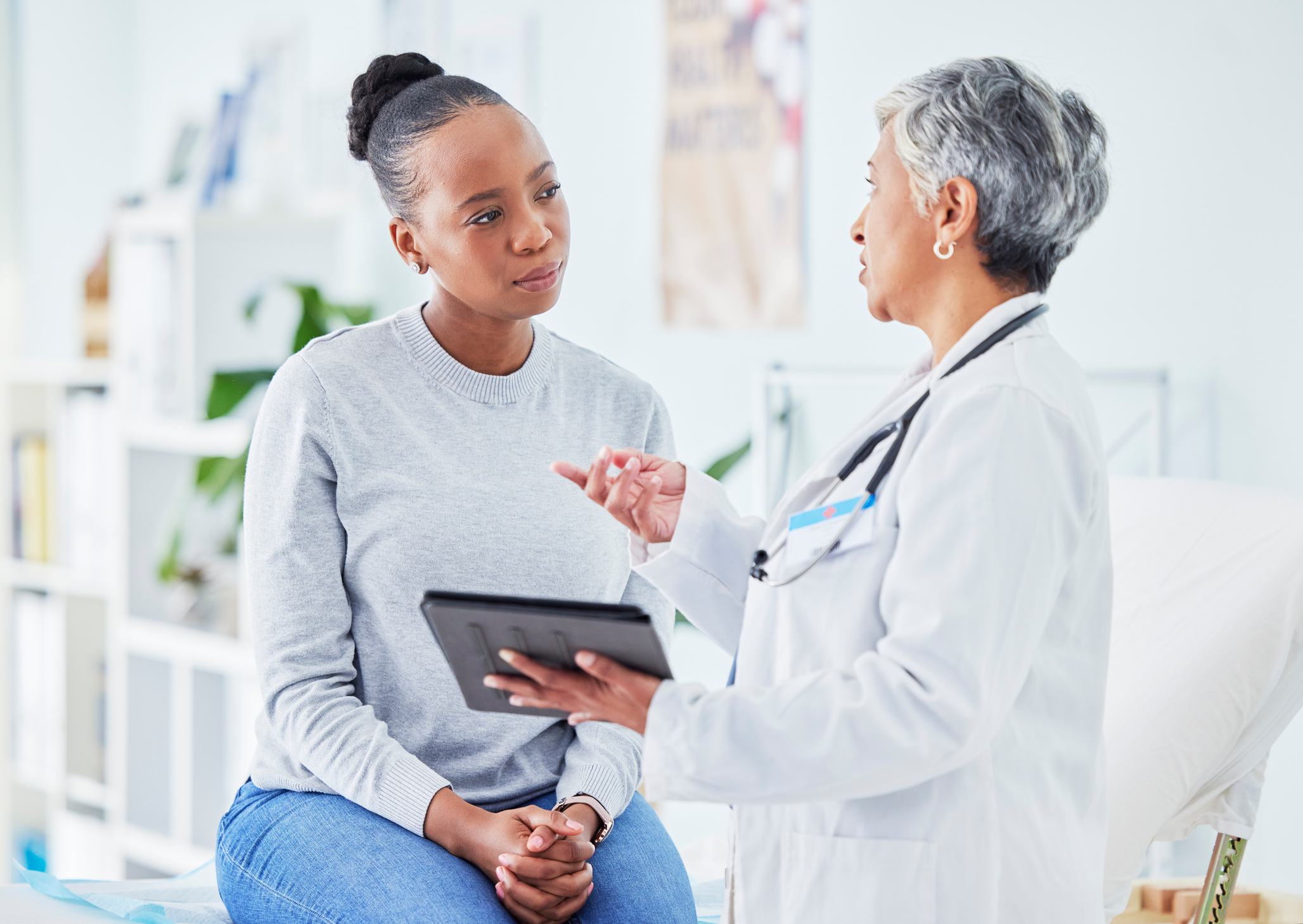 Middle-aged woman sitting on doctor's table while speaking with a woman physician.