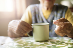 Close up of a senior holding a capsule in one hand and a mug in the other.
