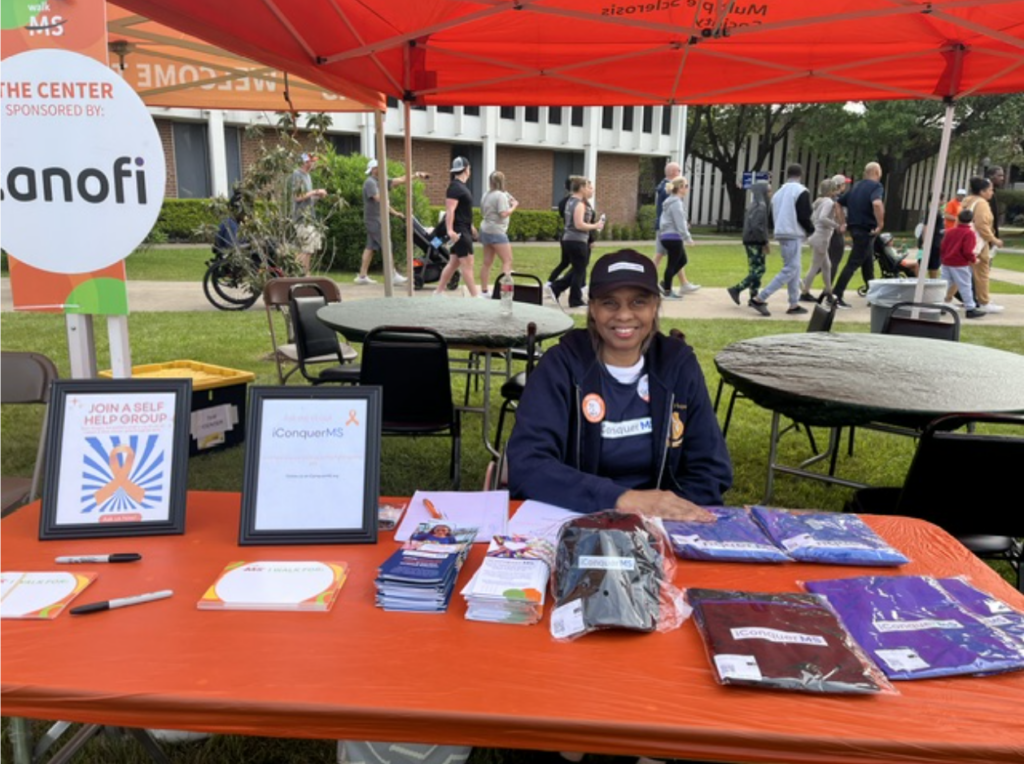 Veronica Daniels-Lewis sitting behind a table under a tent smiling at the Houston MS Walk.