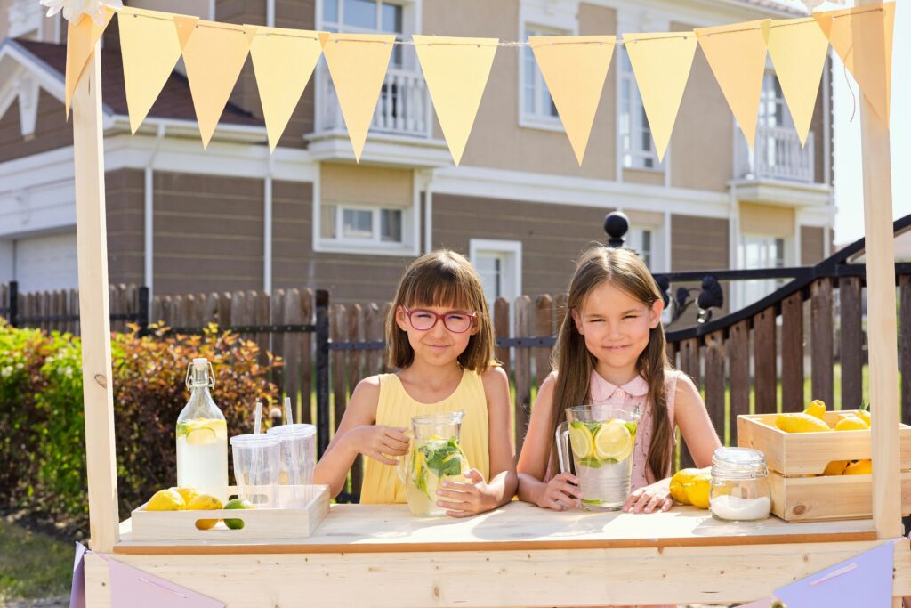 Two young girls selling lemonade at a lemonade stand.