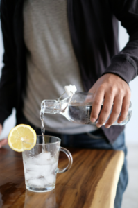 Close up of man pouring water into a glass of ice.