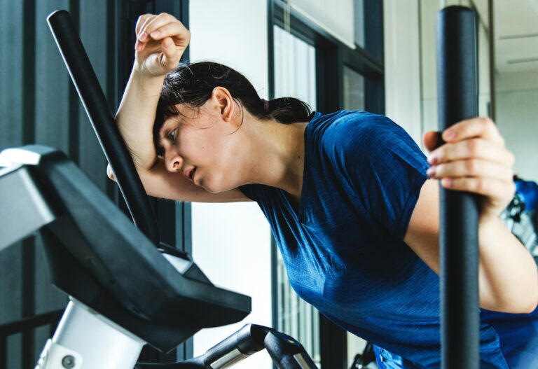 Woman sitting on an exercise bike, taking a break and resting her head on her arm.
