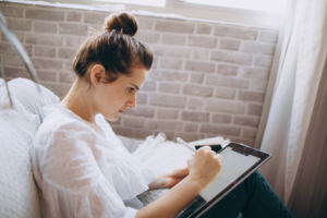 Woman sitting on her couch entering info on a digital tablet