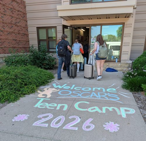 Campers arrive at dorm, with welcome sign written in colorful chalk on the sidewalk