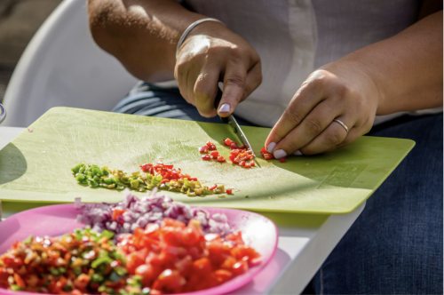 Woman's hands chopping red pepper on a green cutting board, with a plate of chopped veggies next to her.