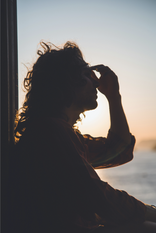 Woman sitting in window, holding brow (seeming to have a headache)
